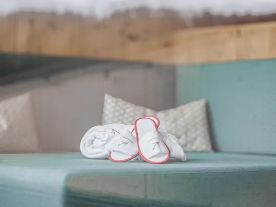 Rolled towel and spa slippers on a teal cushioned bench in a modern wellness hotel